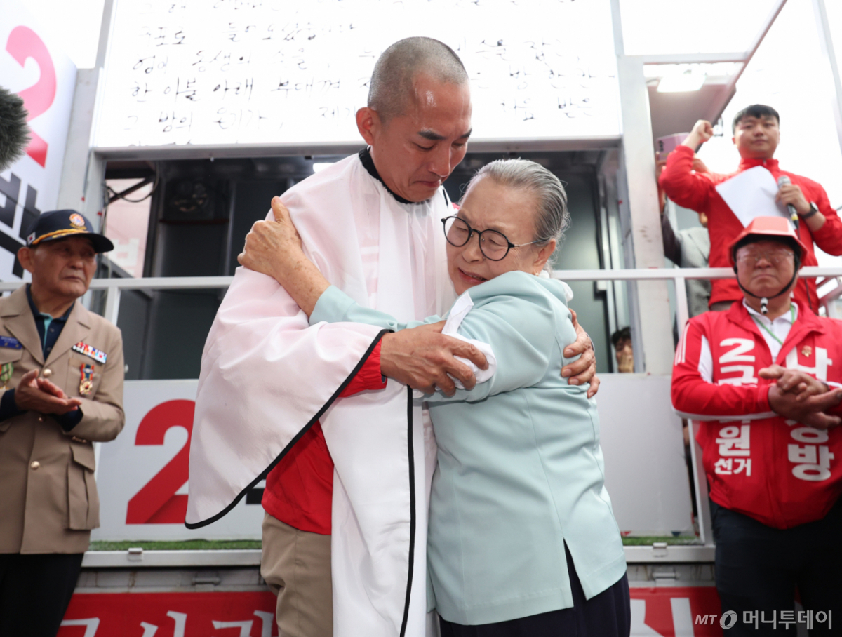 [부산=뉴시스] 김진아 기자 = 제9회 전국동시지방선거 및 국회의원 재·보궐선거의 공식 선거운동이 시작된 21일 박민식 국민의힘 부산 북구갑 국회의원 보궐선거 후보가 부산 북구 구포시장 앞에서 열린 출정식에서 삭발을 한 뒤 자신의 어머니를 안고 있다. 2026.05.21. bluesoda@newsis.com /사진=김진아