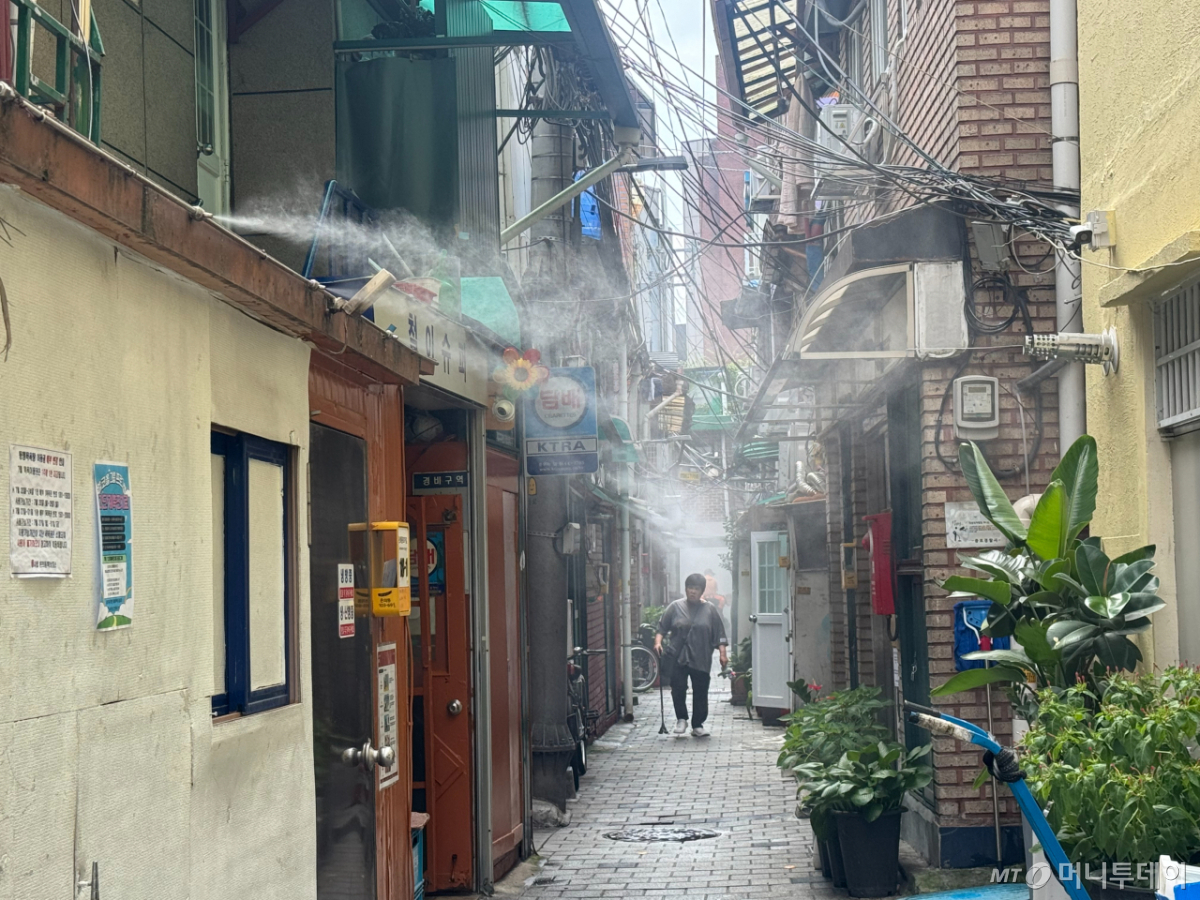 28일 오후 서울 종로구 돈의동 쪽방촌 거리에서 분사되는 쿨링포그 아래를 주민이 지나가고 있다./사진=조유진 기자.