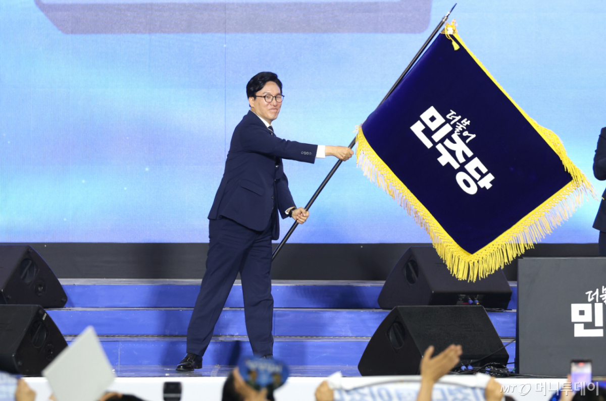 (대전=뉴스1) 황기선 기자 = 김민석 더불어민주당 신임 대표가 17일 대전 유성구 대전컨벤션센터(DCC) 제2전시장에서 열린 제3차 정기전국당원대회에서 당기를 흔들고 있다. (공동취재) 2026.8.17/뉴스1 Copyright © 뉴스1. All rights reserved. 무단 전재 및 재배포, AI학습 이용 금지. /사진=(대전=뉴스1) 황기선 기자