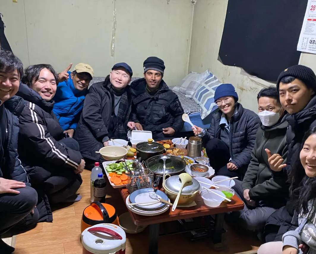 2023년 12월 경기 포천시 한 채소농장의 컨테이너 기숙사에서 이주노동자들과 김달성 목사(왼쪽에서 네번째), 내국인들이 함께 모여 식사하는 모습. /사진제공=포천이주노동자센터.