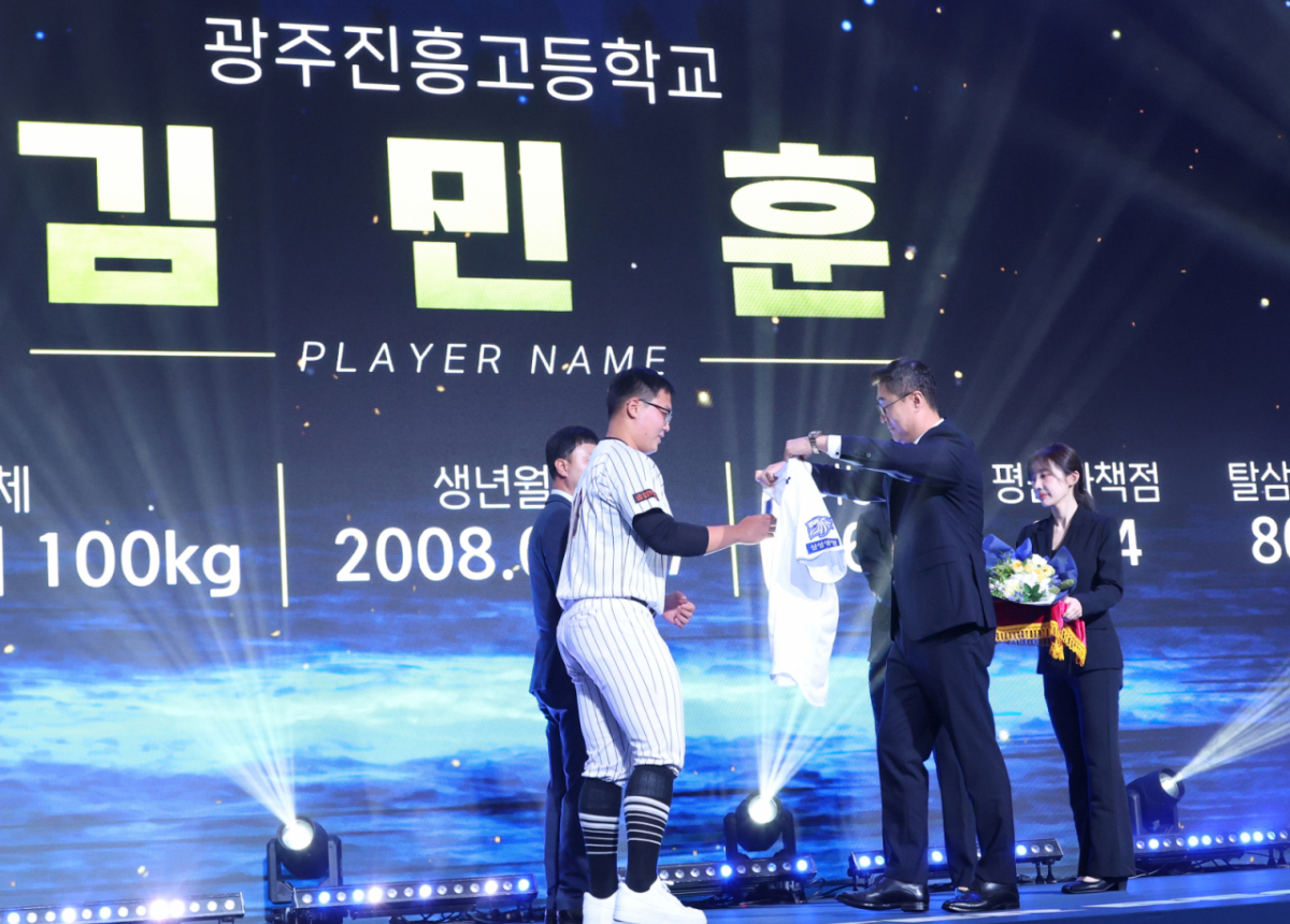 '2027 KBO 신인 드래프트'가 21일 서울 송파구 롯데호텔 월드 크리스탈볼룸에서 열렸다.  김민훈(광주진흥고)이 전체 7순위로 삼성에 지명된 후 이종열 단장의 도음으로 삼성 유니폼을 입고 있다. /사진=김진경 대기자