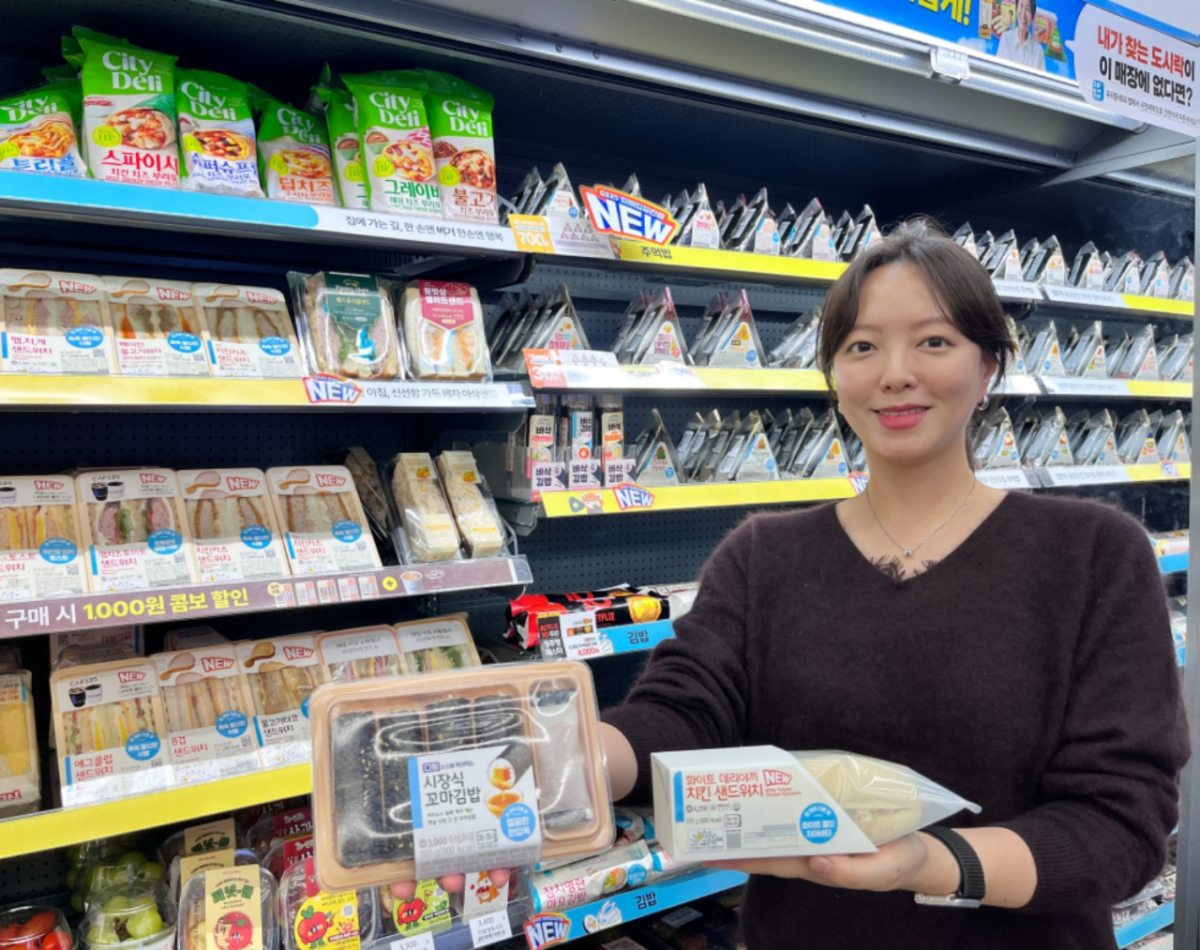 GS25에서 모델이 시장식 꼬마김밥과 화이트 데리야끼 치킨 샌드위치를 들고 포즈를 취하고 있다./사진제공=GS리테일